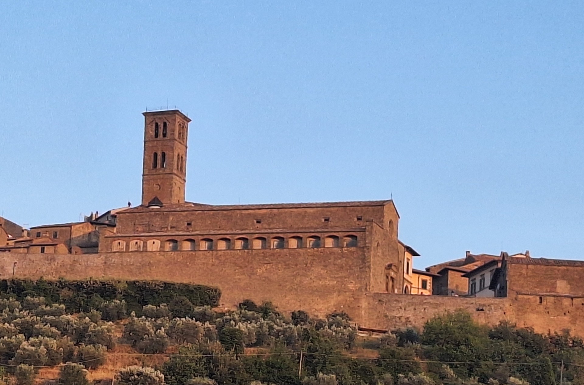 La cattedrale di Cortona e la piazza del Duomo con la pavimentazione in pietra, in luce calda.