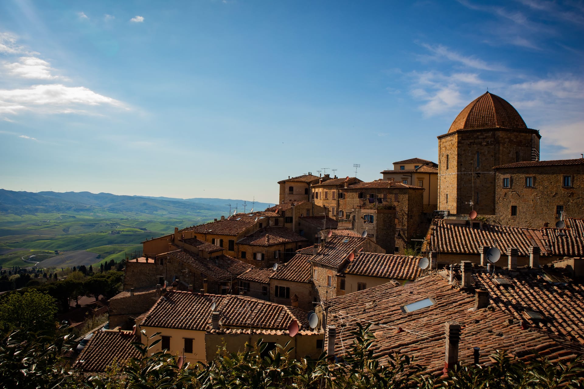 Il borgo medievale di Cortona sulla collina toscana al tramonto, con uliveti e cipressi