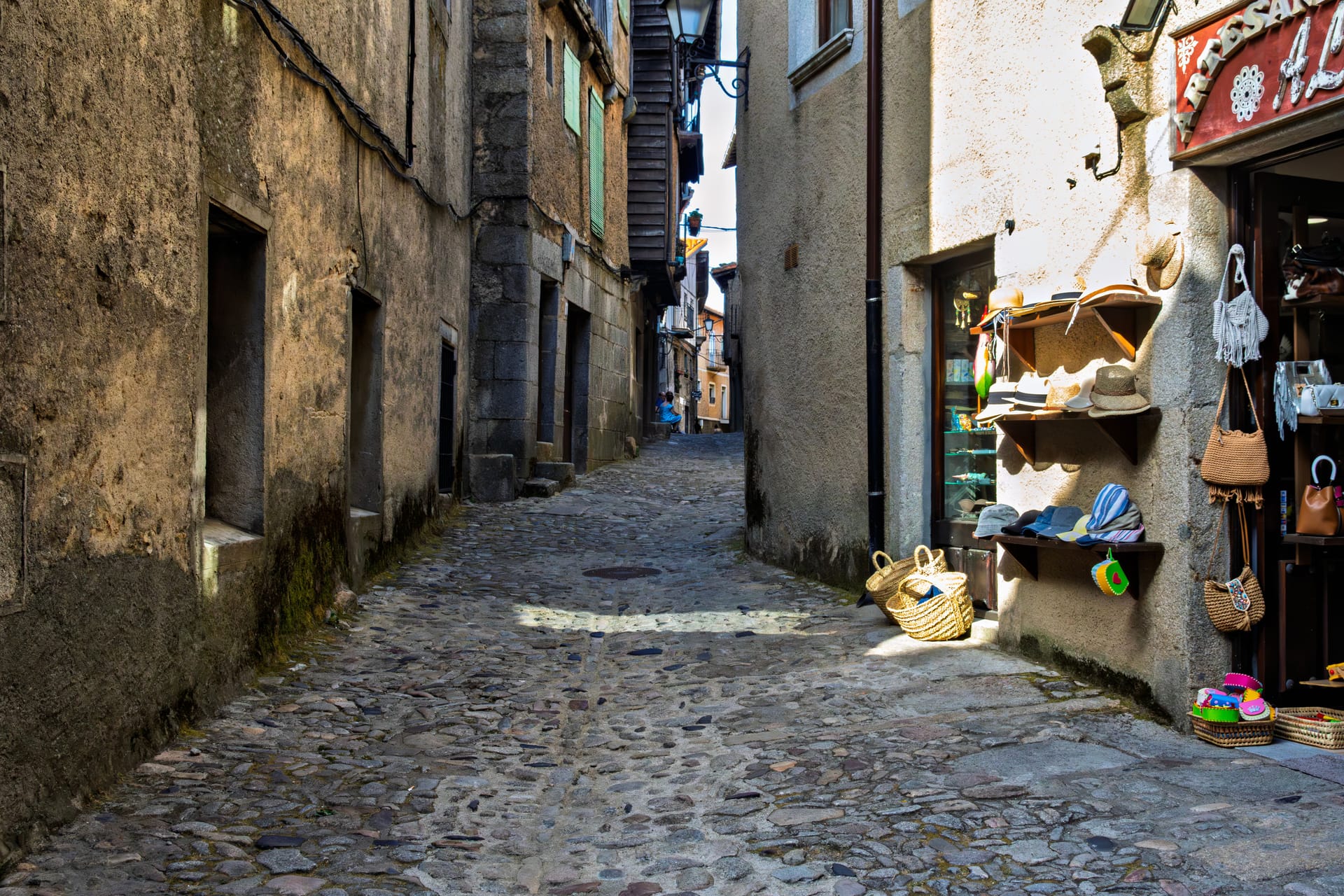 Stretta via in salita nel centro storico di Cortona con botteghe artigiane e muri in pietra